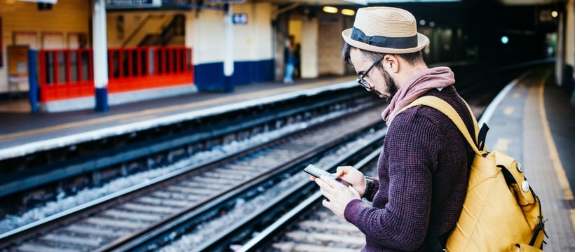 tourisme Un homme attend sur le quai d'une gare smartphone à la main