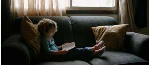 petite fille blonde qui lit un livre sur un canapé