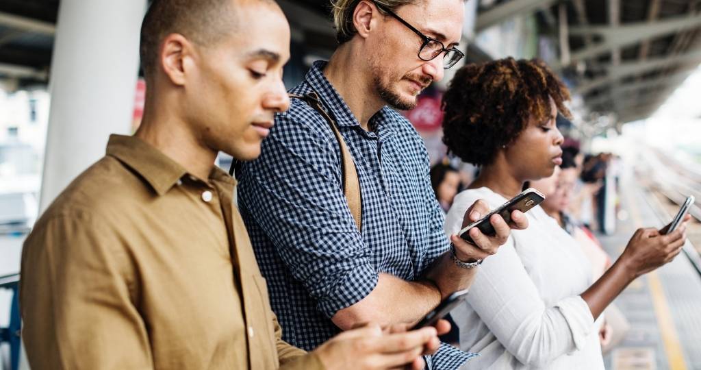 Deux hommes et une femme qui regardent leur smartphone en attendant un train