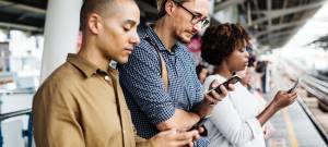 Deux hommes et une femme qui regardent leur smartphone en attendant un train