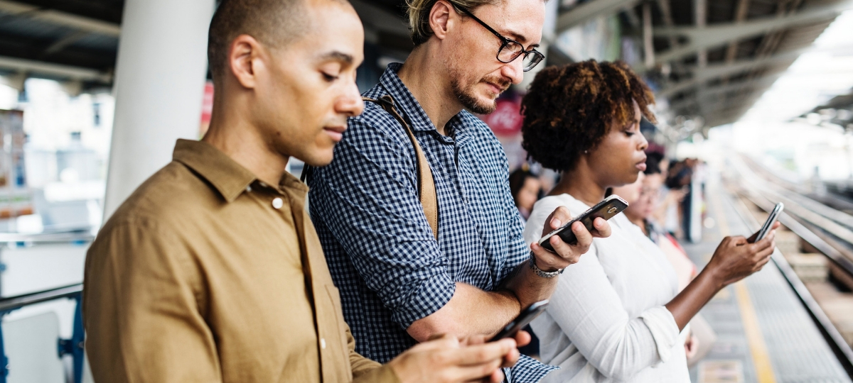 71% des médias d'informations se fait sur mobile Deux hommes et une femme qui regardent leur smartphone en attendant un train
