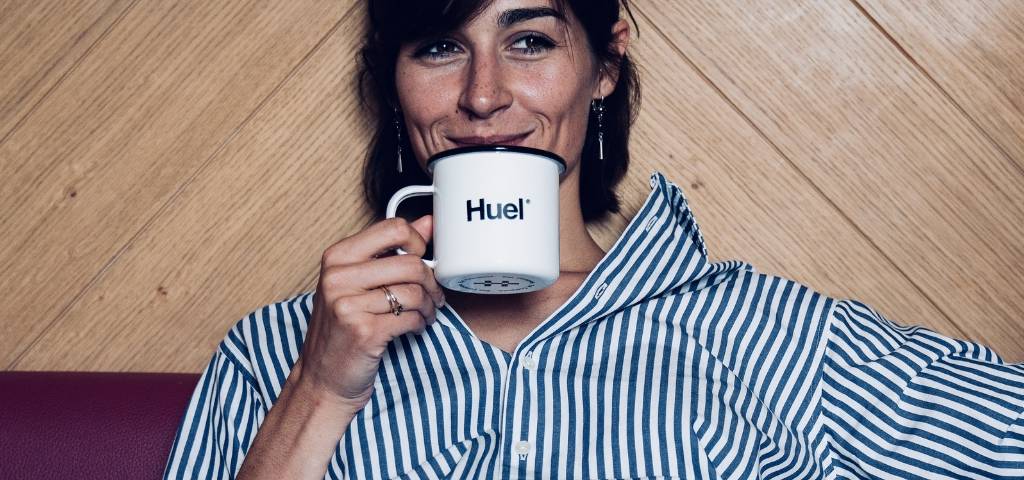 Une femme qui boit dans une tasse avec écrit Huel