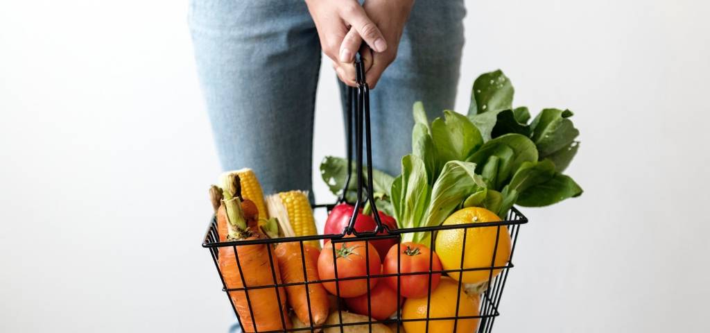 Une personne qui tient un panier de supermarché rempli de fruits et légumes