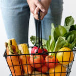 Une personne qui tient un panier de supermarché rempli de fruits et légumes