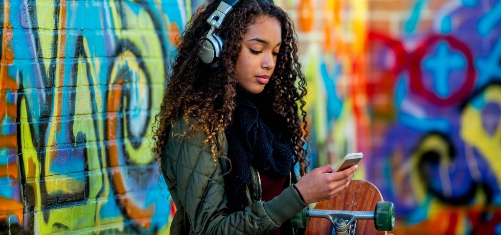 Savez-vous parler aux Zillennials ?  Une adolescente avec un casque sur les oreilles qui regarde son téléphone