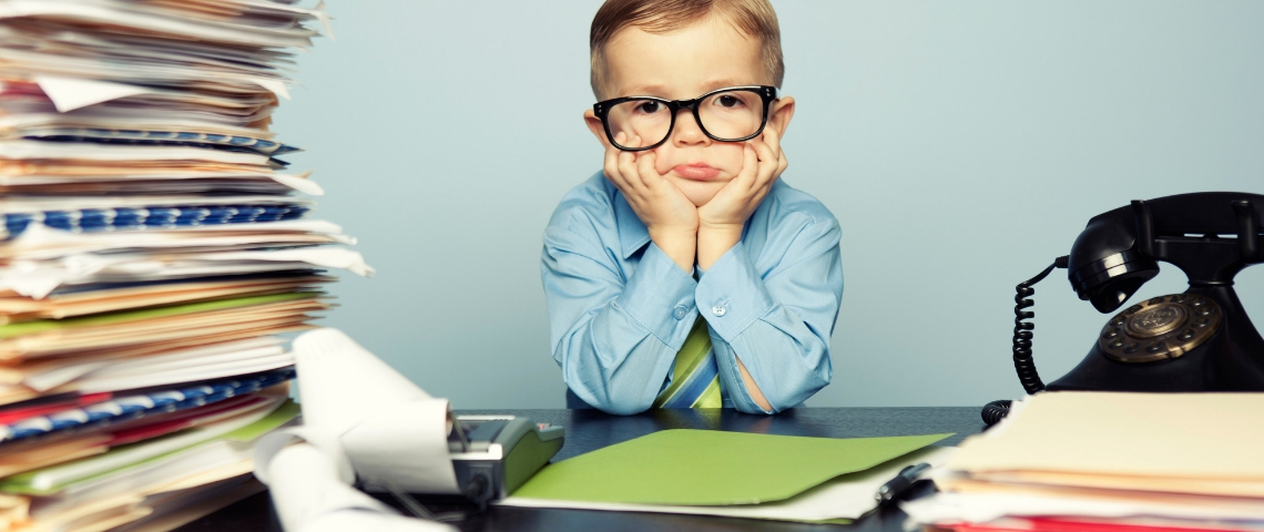 Les 5 erreurs à ne pas commettre pour votre parcours collaborateur Un enfant avec des lunettes assis à un bureau avec une pile de dossiers