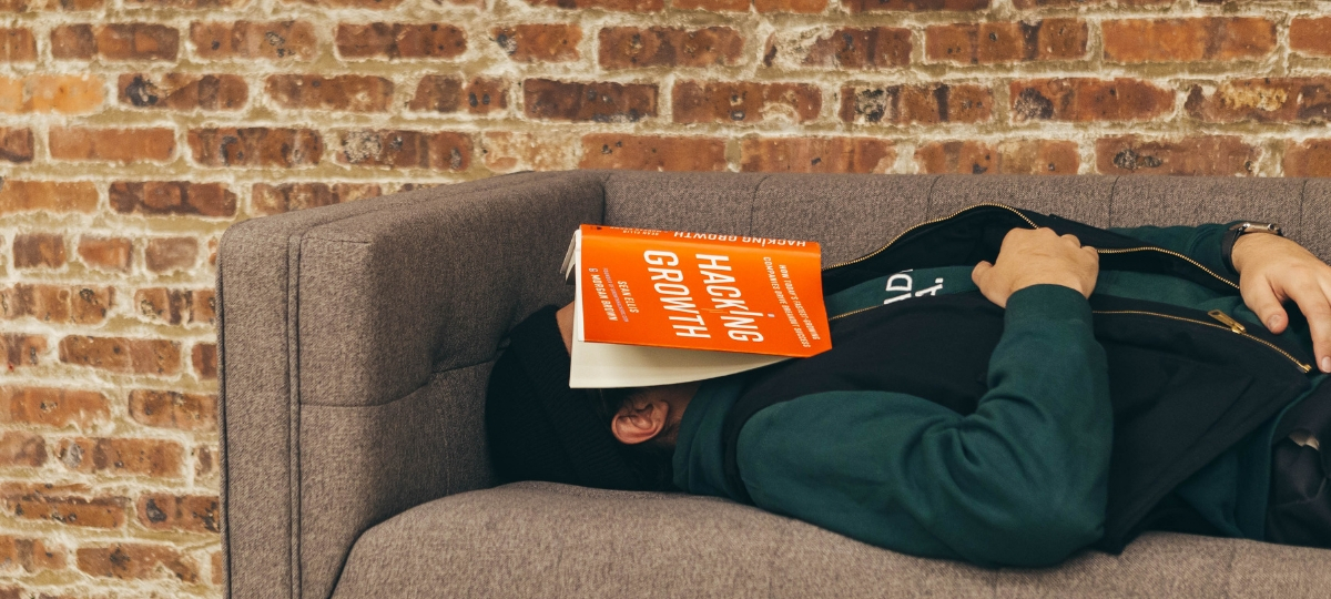 Les Français, rois de la procrastination ? Un homme qui dort sur un canapé avec un livre sur la tête
