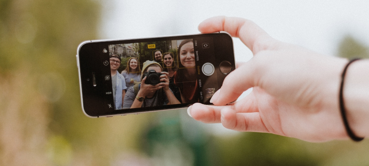 3 pistes pour une nouvelle influence Une main qui tient un smartphone en train de prendre un photo un groupe de personnes
