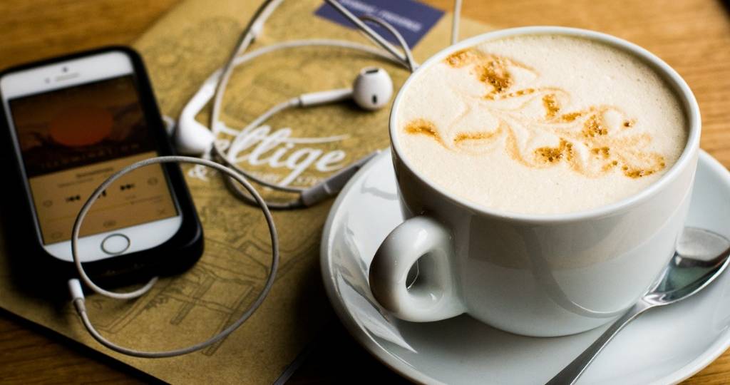 Tasse de cappuccino et smartphone avec des écouteurs sur une table.