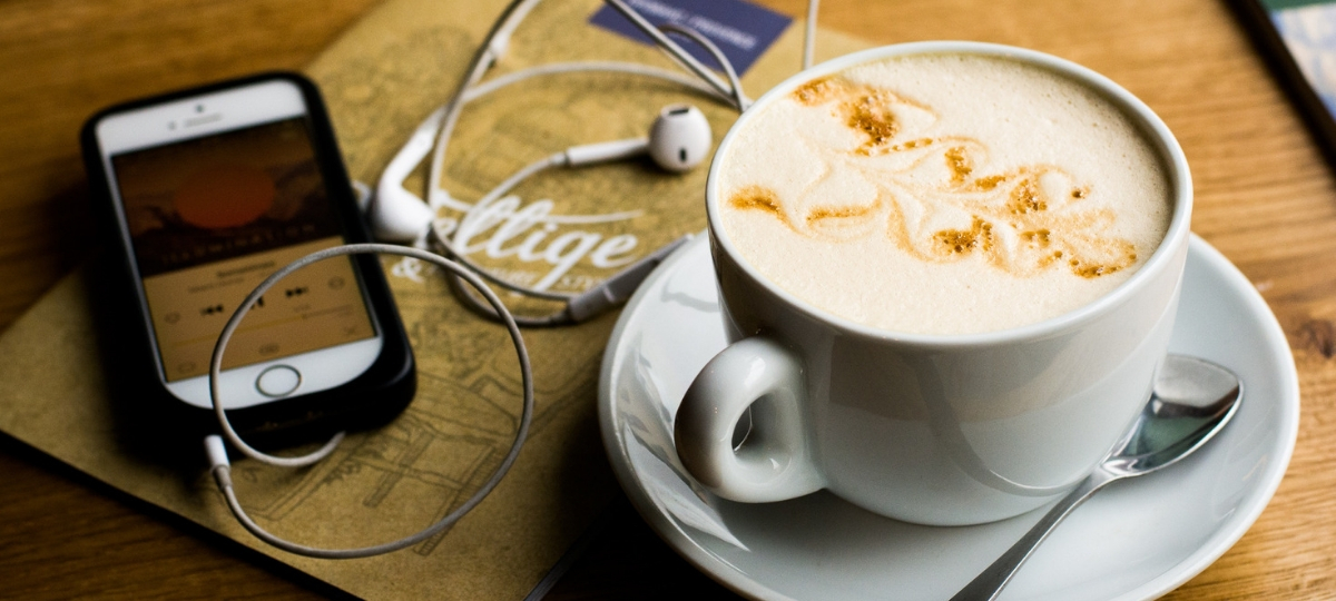 Tasse de cappuccino et smartphone avec des écouteurs sur une table.