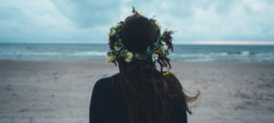 Une femme brune de dos face à la mer avec une couronne de fleurs dans les cheveux
