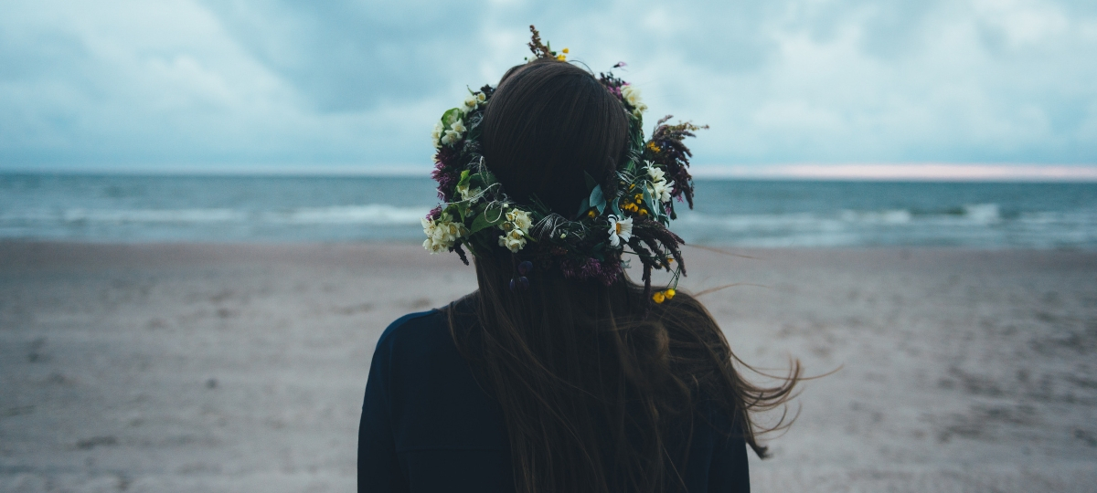 Les entreprises doivent-elles communiquer sur leurs actions RSE ? Une femme brune de dos face à la mer avec une couronne de fleurs dans les cheveux