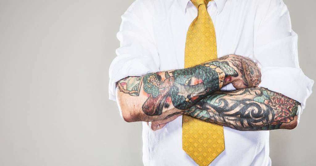 Un homme avec un cravate jaune et des tatouages sur les bras