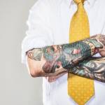 Un homme avec un cravate jaune et des tatouages sur les bras