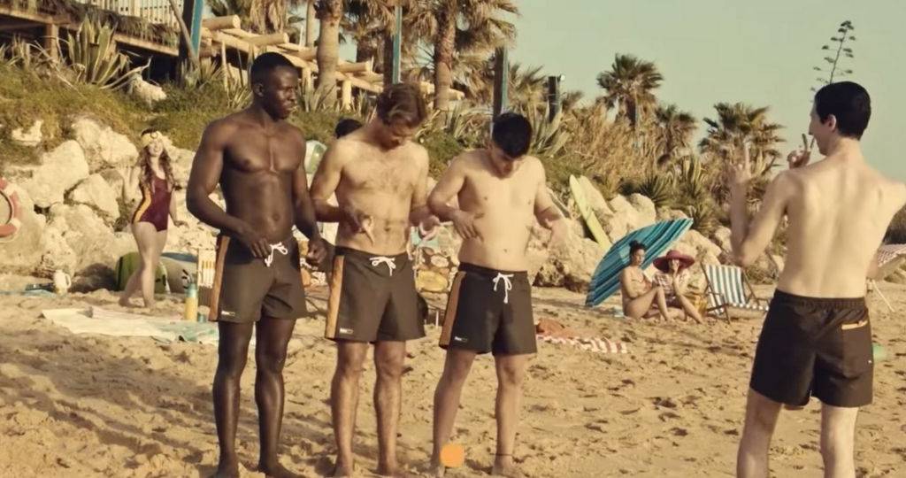 Trois hommes sur une plage, portent des maillots Pornhub
