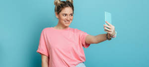 Une femme avec un t-shirt rose qui prend un selfie devant un fond bleu