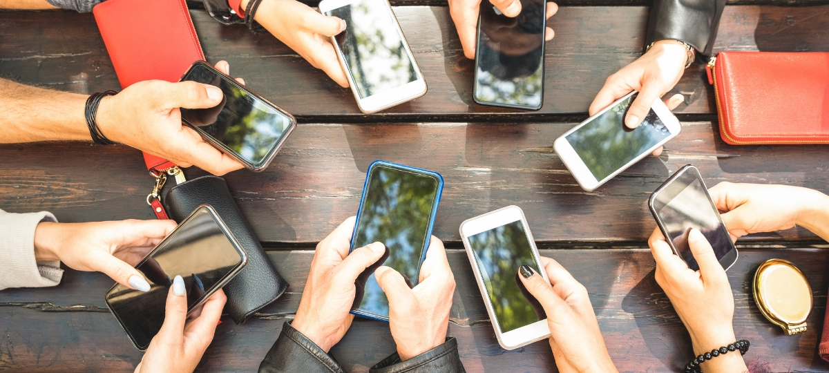Comment gérer sa marque à l'ère de l'industrialisation des réseaux sociaux ? Des mains avec des smartphones autour d'une table