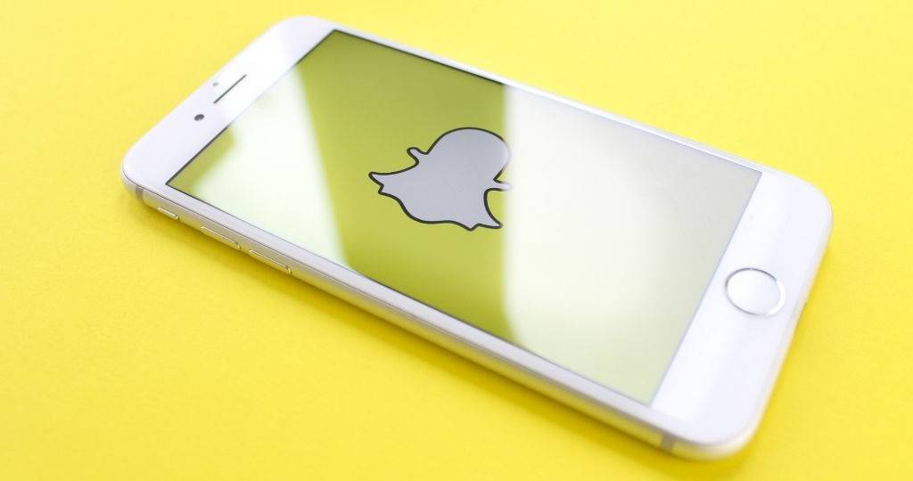Un smartphone posé sur un fonsd jaune, avec sur son écran le logo du réseau social Snapchat