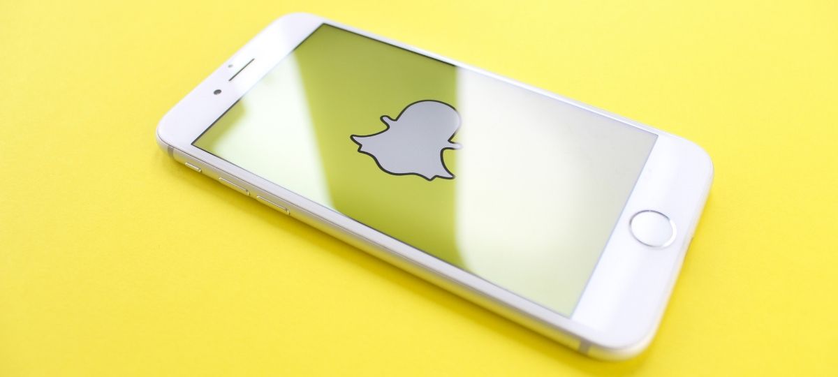 Un smartphone posé sur un fonsd jaune, avec sur son écran le logo du réseau social Snapchat
