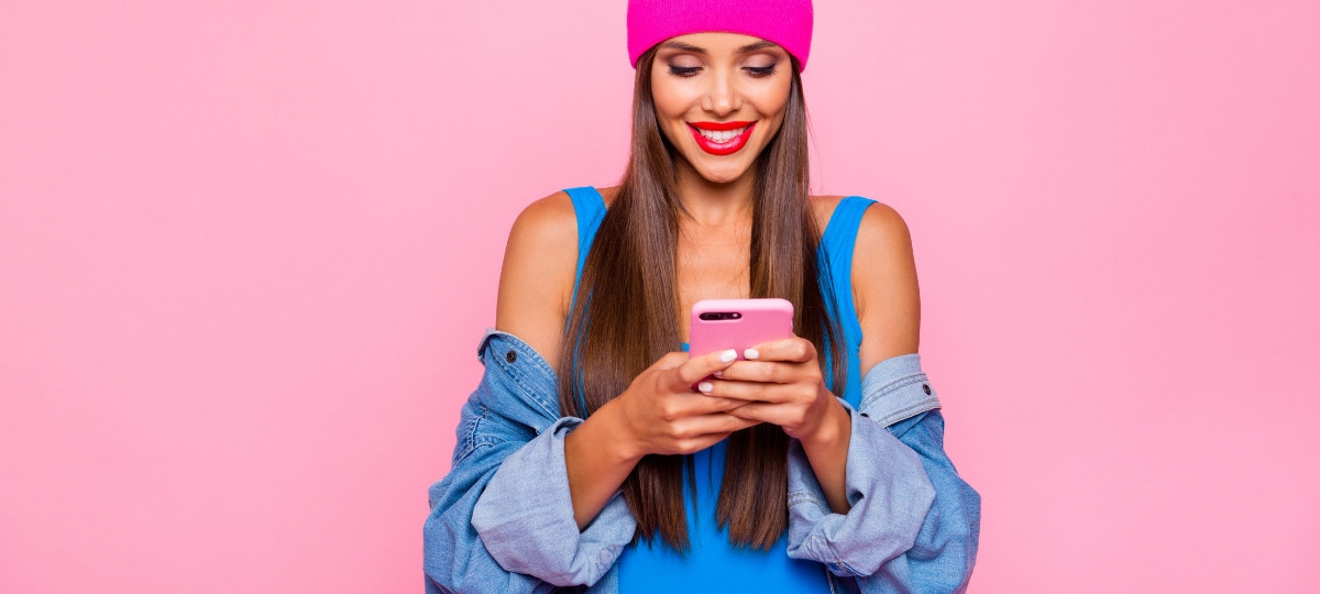 3 raisons de miser sur la messagerie instantanée Une femme en train d'écrire sur son smartphone devant un fond rose