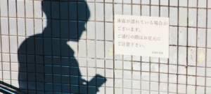 Ombre d'un homme tenant son téléphone, sur le coté une affiche japonaise