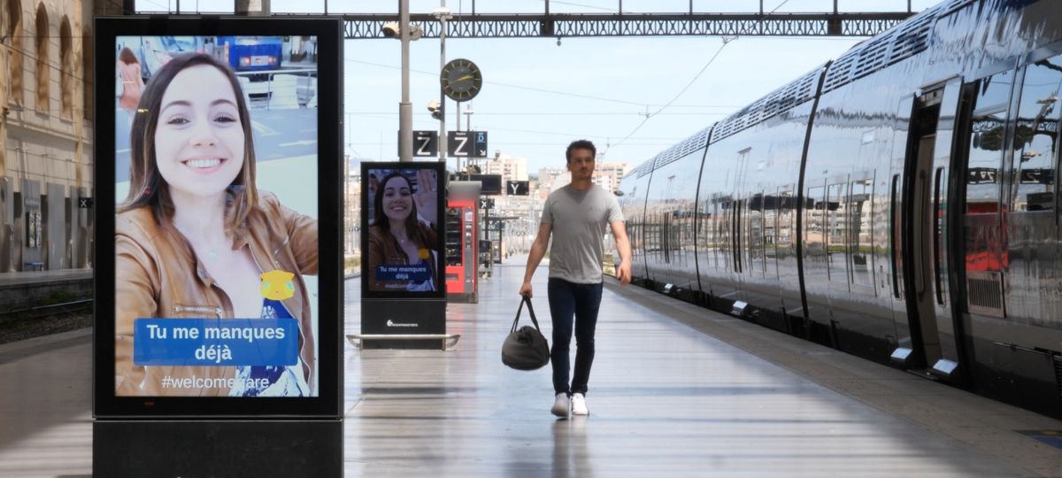 Mediagare prolonge les aurevoirs Un homme regarde sa petite amie qui lui laisse un message sur les panneaux digitaux d'une gare