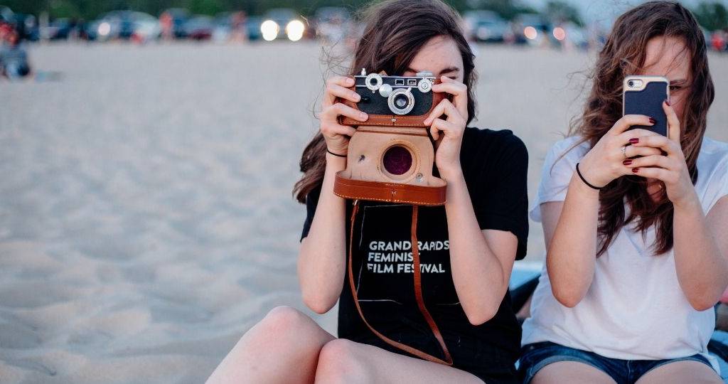 Deux jeunes adolescentes prennent des photos à la plage sur leur téléphone et un appareille photo