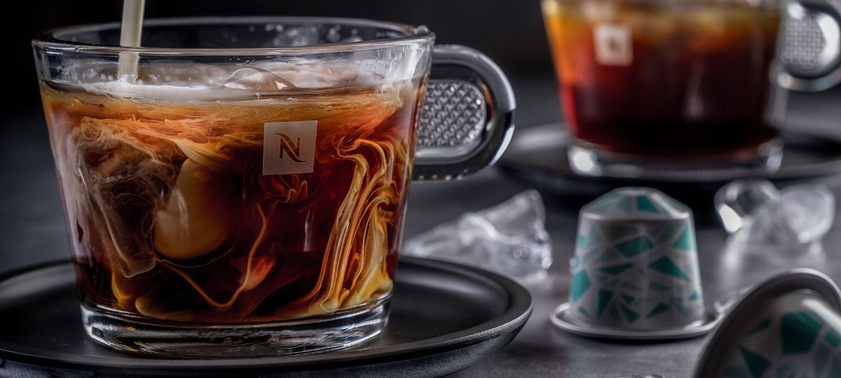 Nespresso déploie un système de recyclage pour ses capsules Sur une table se trouve une tasse de café Nespresso dans laquelle on verse un nuage de lait. A gauche, une capsule Nespresso