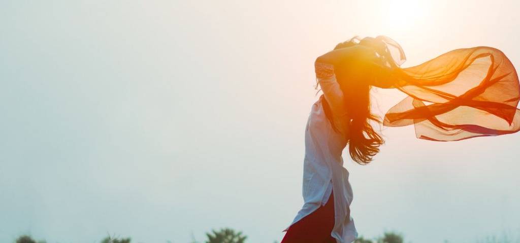 Viusle d'une femme les bras en l'air au soleil levant