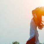 Viusle d'une femme les bras en l'air au soleil levant