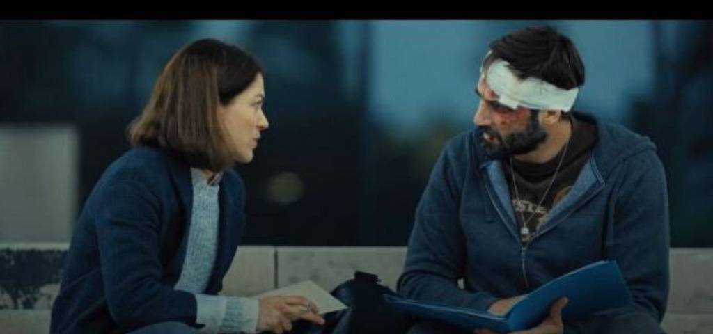 Une femme et un homme discutte assis sur un banc. L'homme a un bandage autour de la tête