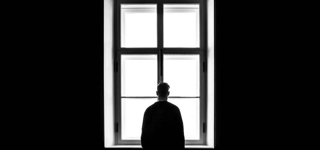 Visule d'un homme seul devant une fenêtre regardant à l'horizon
