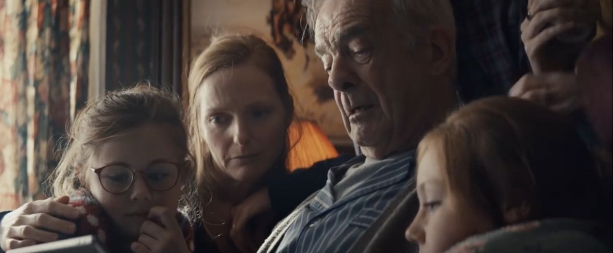 Apple dévoile sa traditionnelle pub de Noël pleine d’émotions Capture de la publicité d'Apple ppur Noël, avec une famille réunit en trai nde regarder un diaporama sur l'Ipad