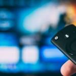 Personne tenant une télécommande dans sa main devant un écran