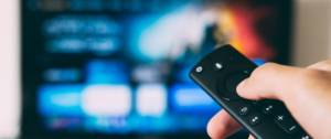 Personne tenant une télécommande dans sa main devant un écran