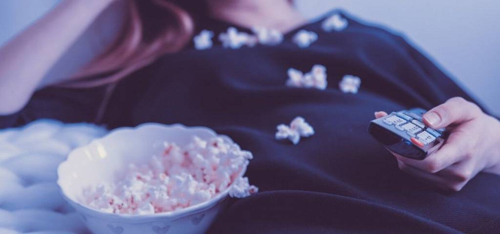 Jeune mangeant du pop-corn, allongé sur son lit, avec une télécommande à la main