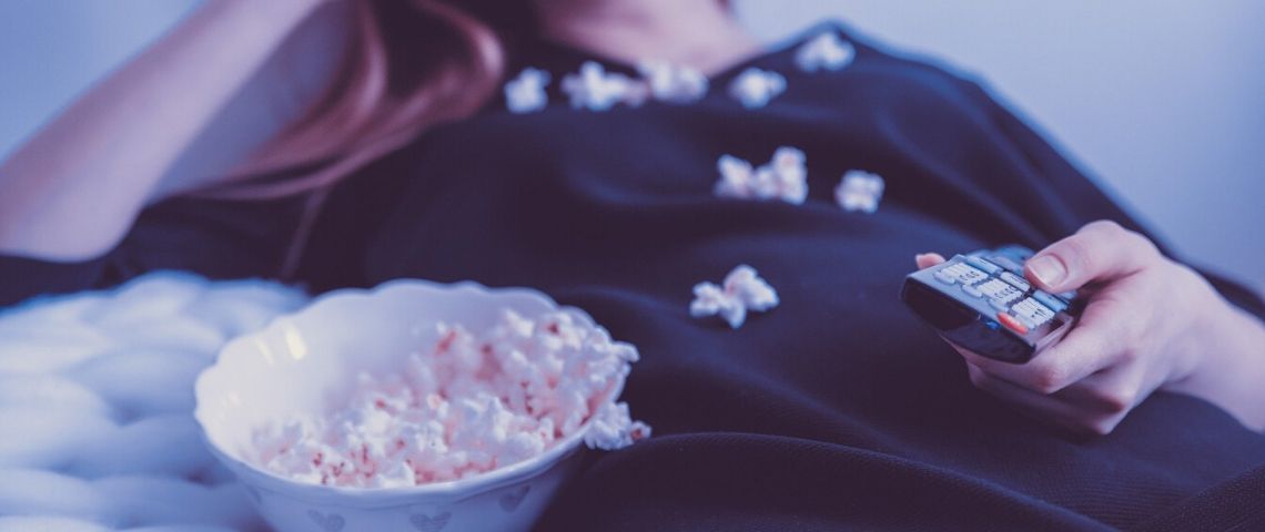 Netflix lance le top 10 des films et séries les plus populaires Jeune mangeant du pop-corn, allongé sur son lit, avec une télécommande à la main