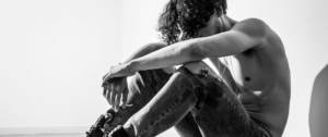 Homme torse nu, assis, la tête entre ses bras