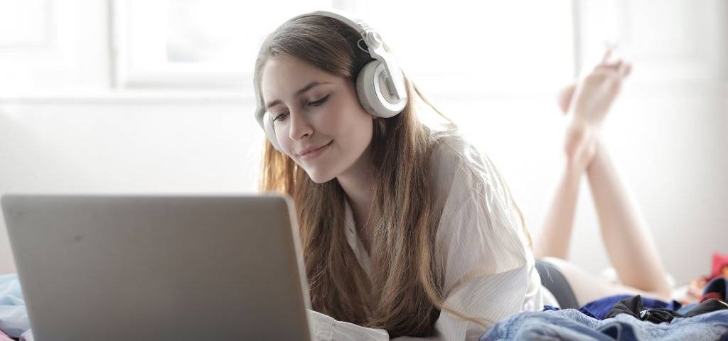 Jeune fille allongée sur son lit, devant un ordinateur avec un casque sur les oreilles