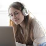 Jeune fille allongée sur son lit, devant un ordinateur avec un casque sur les oreilles