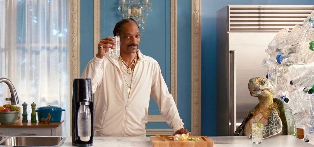 A l’occasion des fêtes de fin d’année Sodastream et Snoop Dogg vous souhaitent un joyeux noël 2020 Snoop Dogg, un verre de sodastream à la main avec une tortue et des déchets de bouteilles plastiques derrière elle