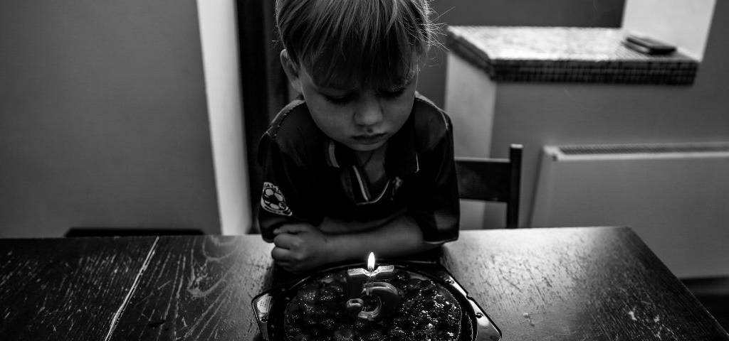 Photo en noir et blanc, d'un enfant assis seule, devant un gateau, avec une bougie pour ses 5 ans