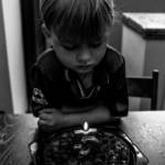 Photo en noir et blanc, d'un enfant assis seule, devant un gateau, avec une bougie pour ses 5 ans