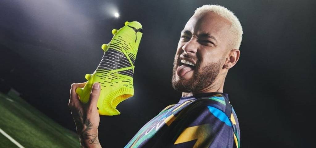 Neymar Jr. avec une basket jaune fluo dans la main et tirant la langue