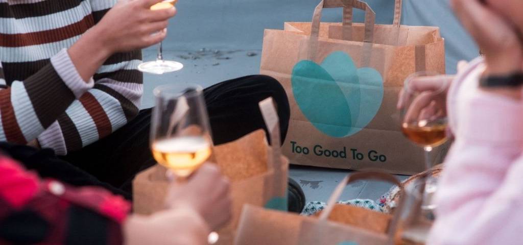 Personne partageant un déjeuner, avec des sacs au logo de Too Good To Go