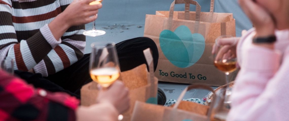 Too Good To Go, l’application de lutte contre le gaspillage alimentaire, continue à développer son mouvement au niveau mondial. Personne partageant un déjeuner, avec des sacs au logo de Too Good To Go