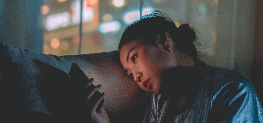 Jeunes fille devant son écran de téléphone portable, avec un air triste