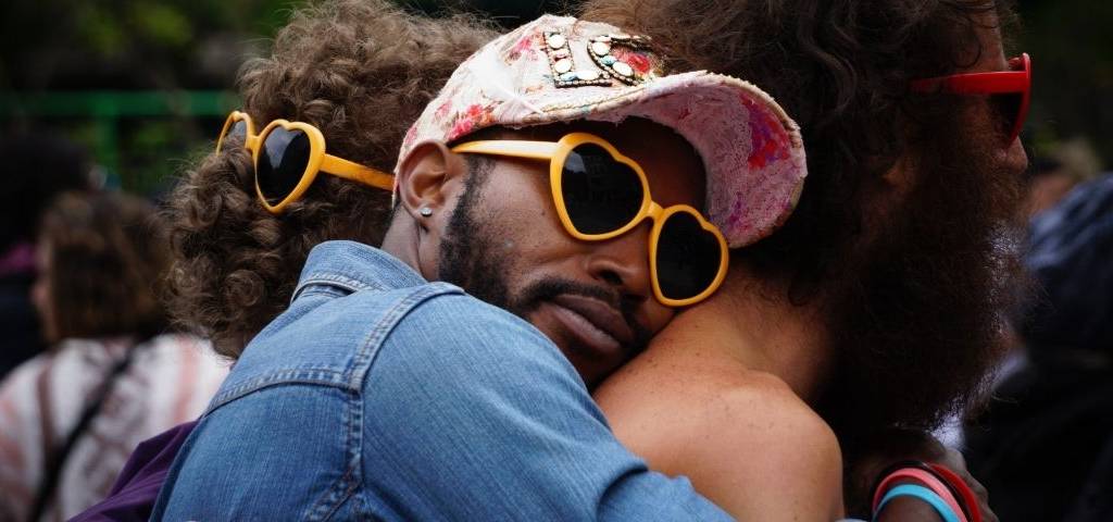 Homme noir avec des lunettes en forme de coeur, serrant dans es bras un homme blanc