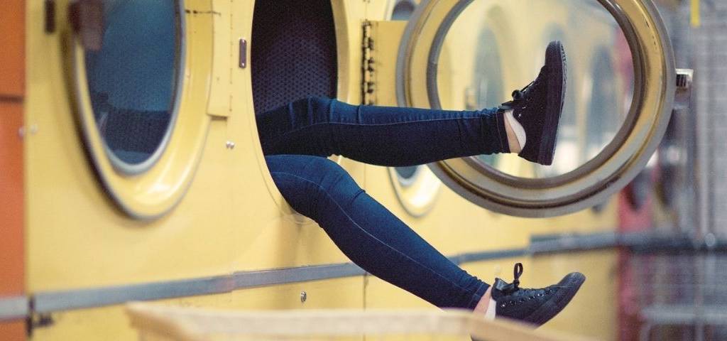 Jeune femme assise dans une machine à laver, laissant dépasser ses 2 jambes