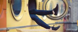 Jeune femme assise dans une machine à laver, laissant dépasser ses 2 jambes